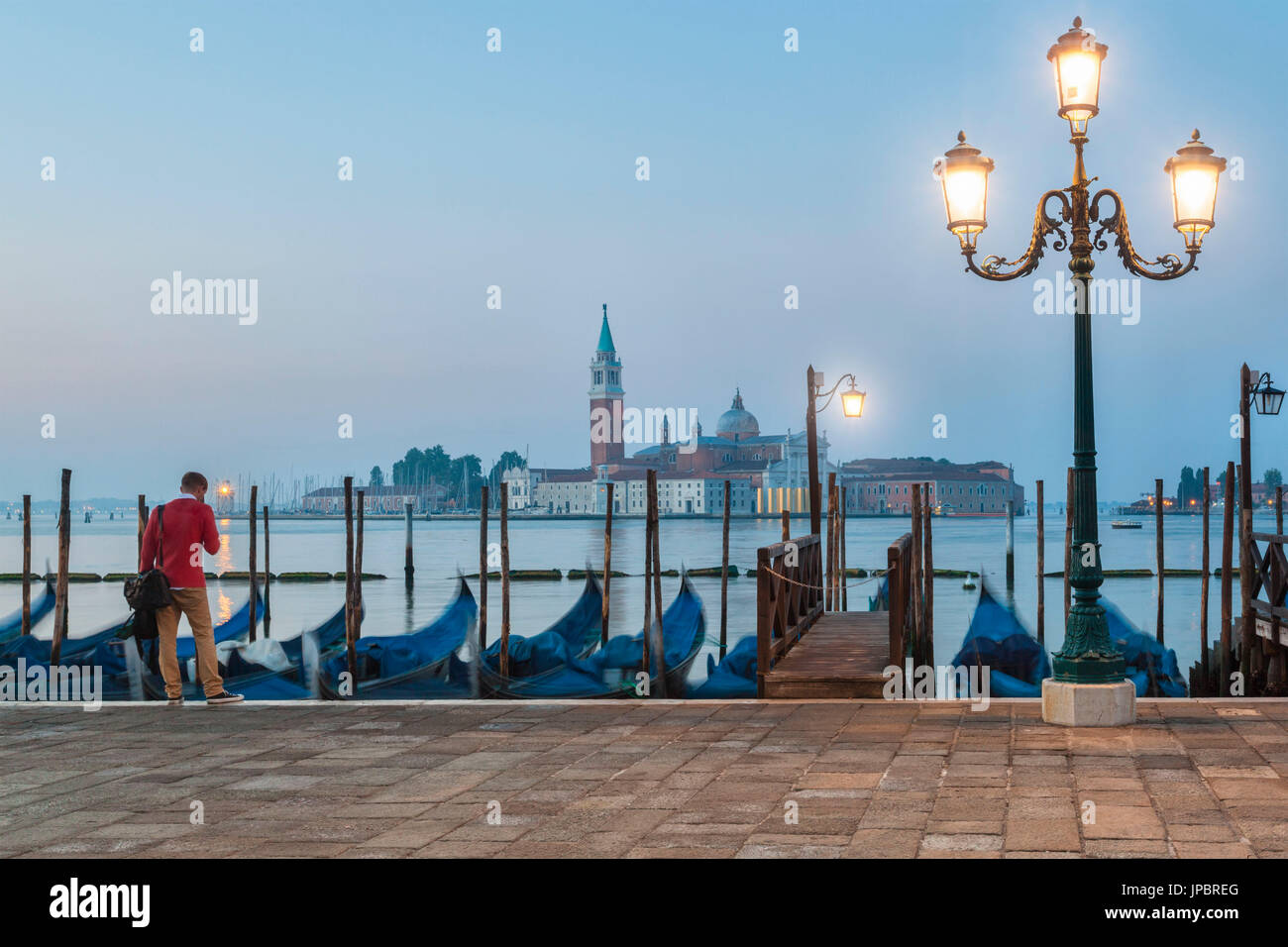 Ein einsamer Mann wartet vor der Gondeln, die entlang der Riva Degli Schiavoni angedockt. im Hintergrund die Insel San Giorgio Maggiore, Venedig, Italien Stockfoto
