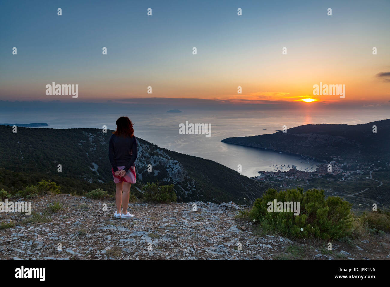 Ein Mädchen sieht die Landschaft und das Dorf von komiza von Hum aus Berg bei Sonnenuntergang (Komiza, Insel Vis, Split-dalmatien County, Dalmatien, Kroatien, Europa) Stockfoto