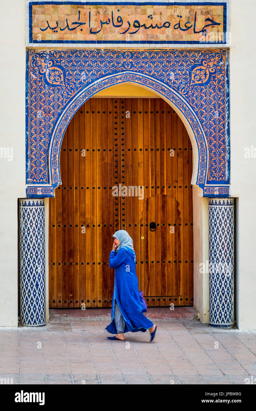 Fes, Marokko, Nordafrika. Frau mit blauen Tracht vor einer typischen marokkanischen Tür. Stockfoto