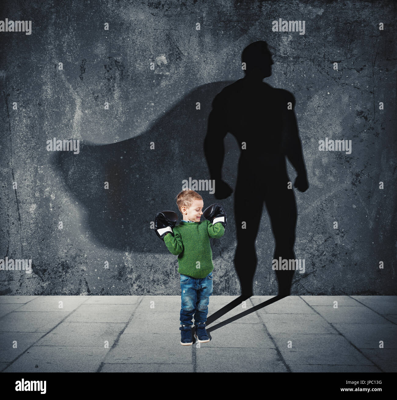 Kleines Kind mit seinem Schatten von Superhelden an der Wand. Stockfoto