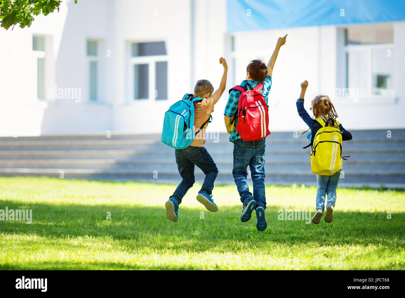 Kinder mit Rucksäcken springen im Park in der Nähe von Schule. Schülerinnen und Schüler mit Büchern und Rucksäcke im freien Stockfoto