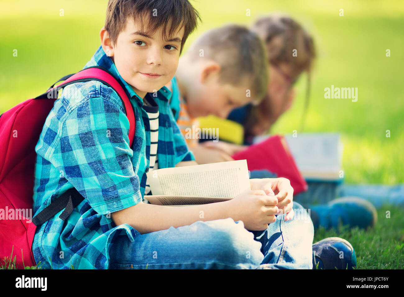 Kinder mit Rucksäcken sitzen im Park in der Nähe von Schule Stockfoto