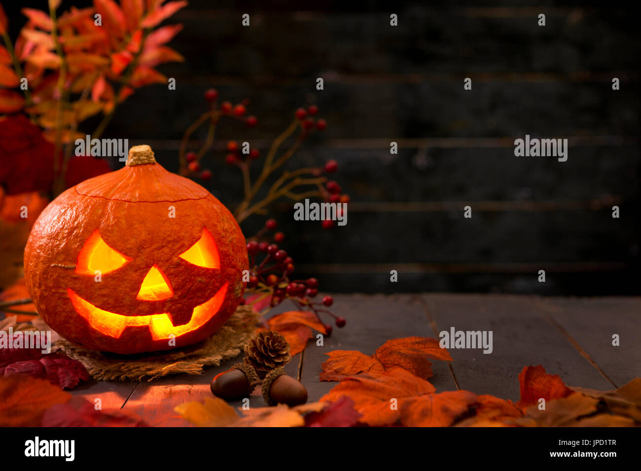 Brennen von Jack O'Lantern auf einem rustikalen Tisch mit herbstlichen Dekorationen, beleuchtet dunkel. Stockfoto