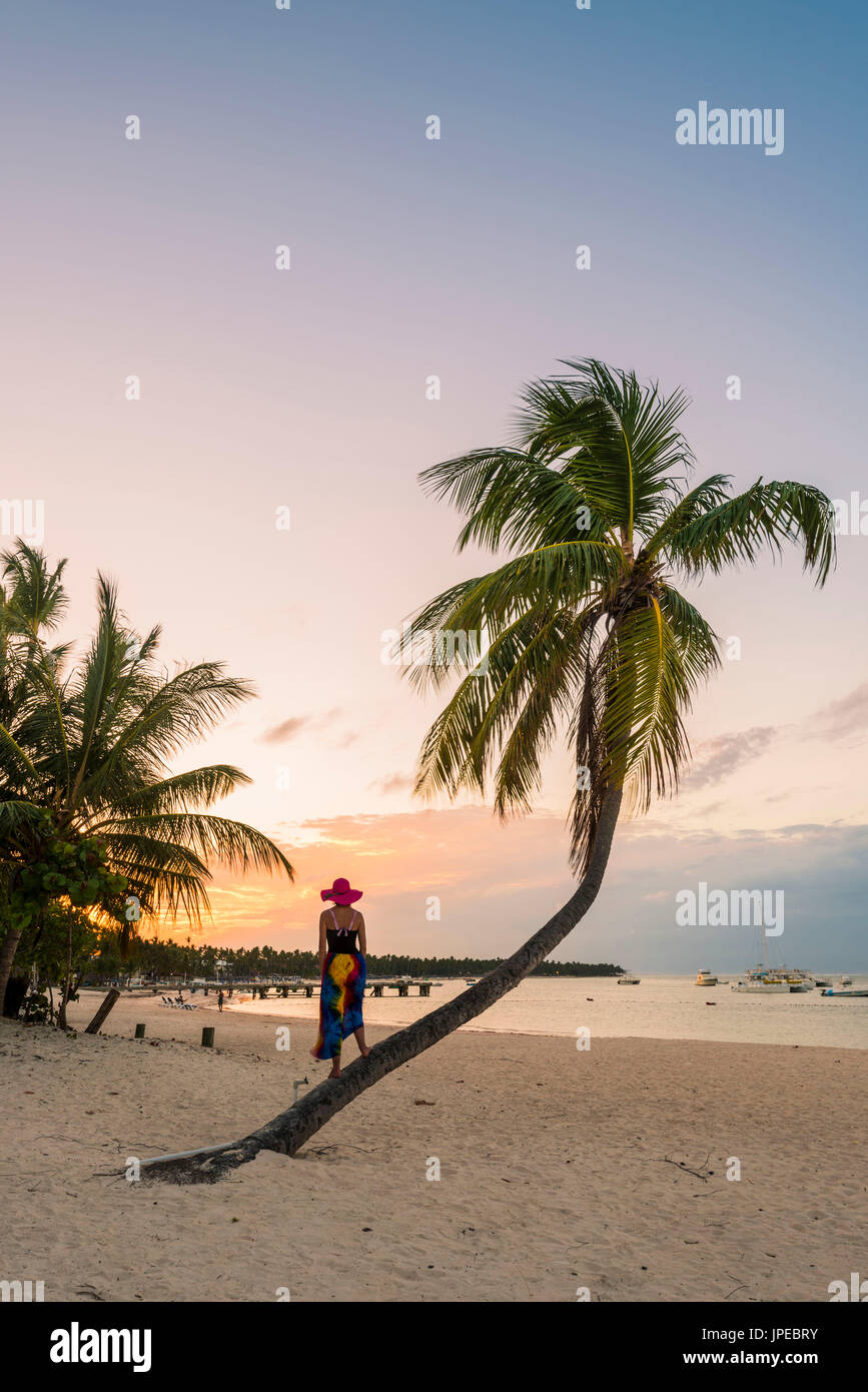 Strand von Cabeza de Toro, Punta Cana, Dominikanische Republik. Frau, die auf dem Stamm einer Palme (MR). Stockfoto