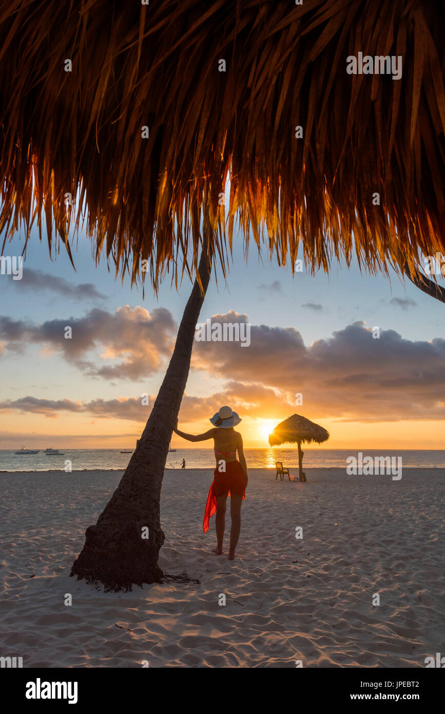 Bavaro Beach, Bavaro, Higuey, Punta Cana, Dominikanische Republik. Frau von Stroh Sonnenschirme am Strand bei Sonnenaufgang (MR). Stockfoto