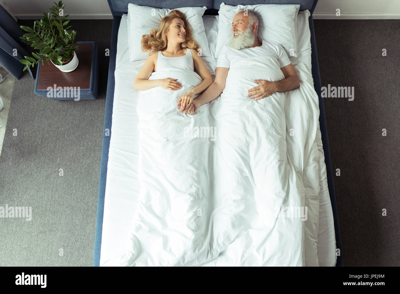 Draufsicht der lächelnde paar im Bett liegend und Hand in Hand zu Hause Stockfoto