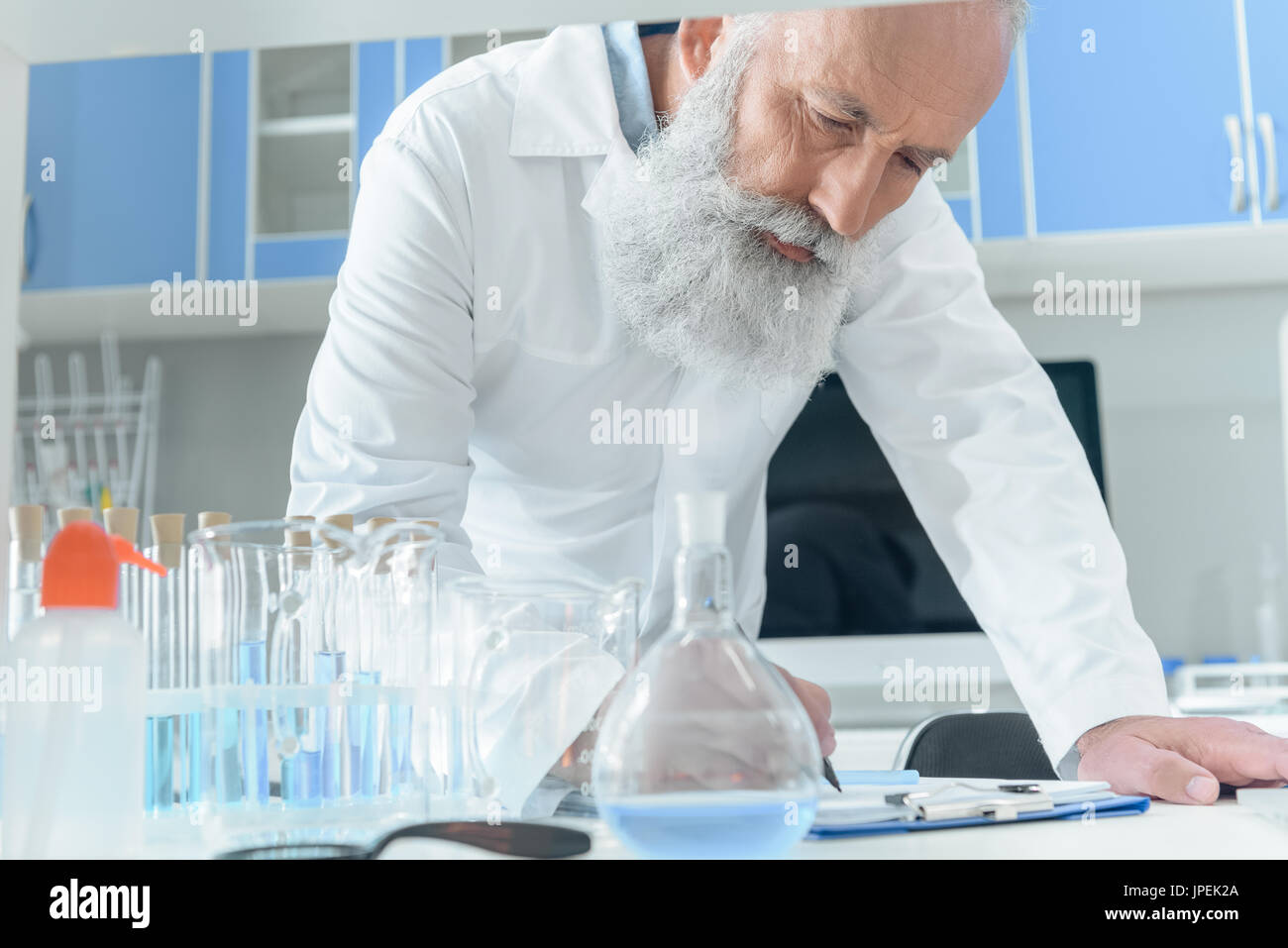 konzentrierte bärtigen wissenschaftlicher Mitarbeiter im weißen Kittel mit Fläschchen im Chemielabor in Zwischenablage Tanle schreiben Stockfoto