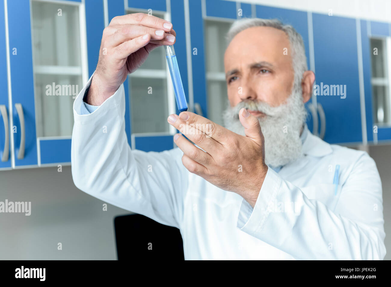 nachdenklich senior bärtigen Chemiker im weißen Kittel halten Rohr mit Reagenz im chemischen Labor Stockfoto