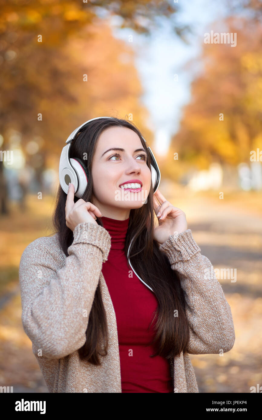 Junge glücklich lächelnde Frau mit Kopfhörer im Freien auf Herbst Tag. Mädchen Musik im Park. Herbst Porträt Stockfoto