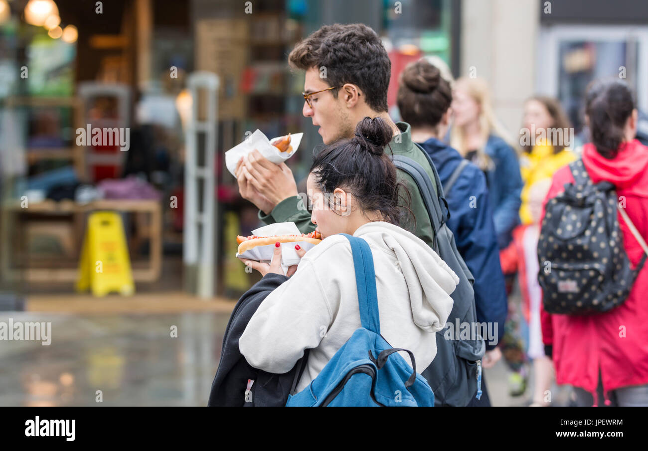 Junges Paar Hotdogs außerhalb in einer Stadt zu essen, während es regnet. Stockfoto