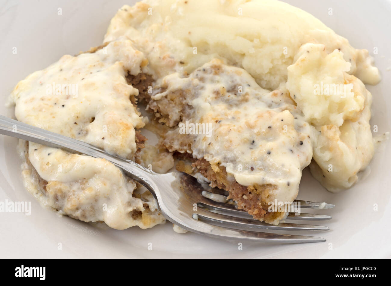 Nahaufnahme von einem gebratenen Rindersteak in Soße mit Kartoffelpüree auf einem Teller mit einer Gabel einstechen. Stockfoto