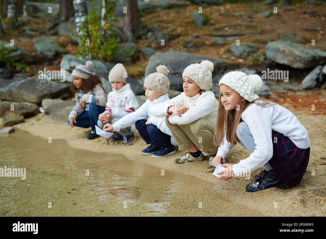 Reihe von Kindern hockt auf Sand entlang am Wasser Stockfoto