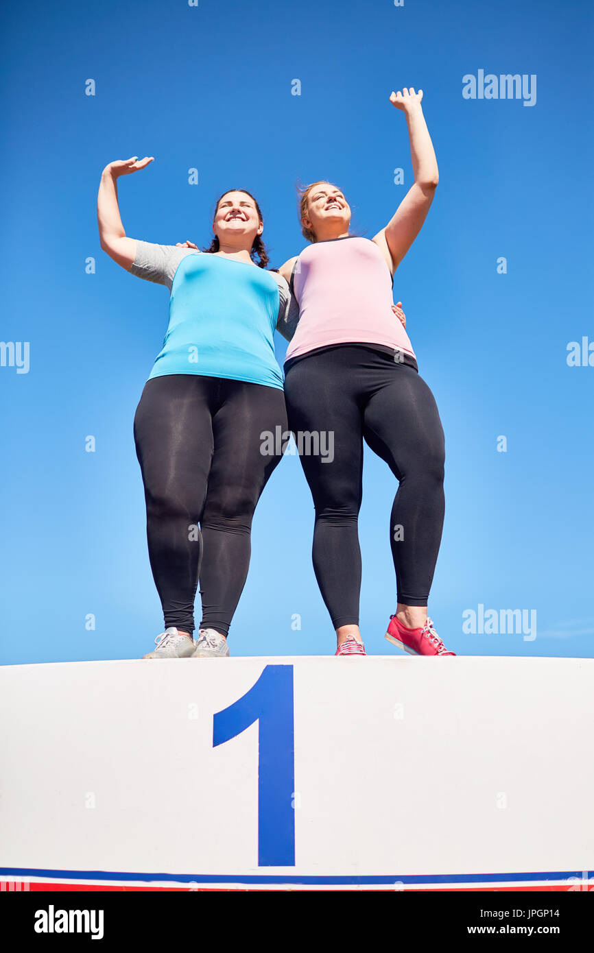 Zwei Plus-Size Frauen stehen auf Podium mit Nummer eins und Gruß fans Stockfoto