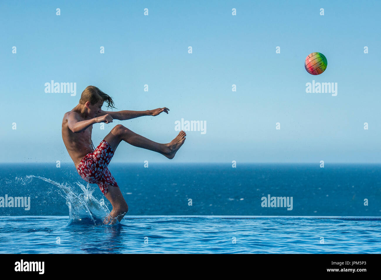 Ein Junge springt ein Ball in ein Infinity Pool im Sommer zu treten, Fußball spielen im Urlaub Stockfoto