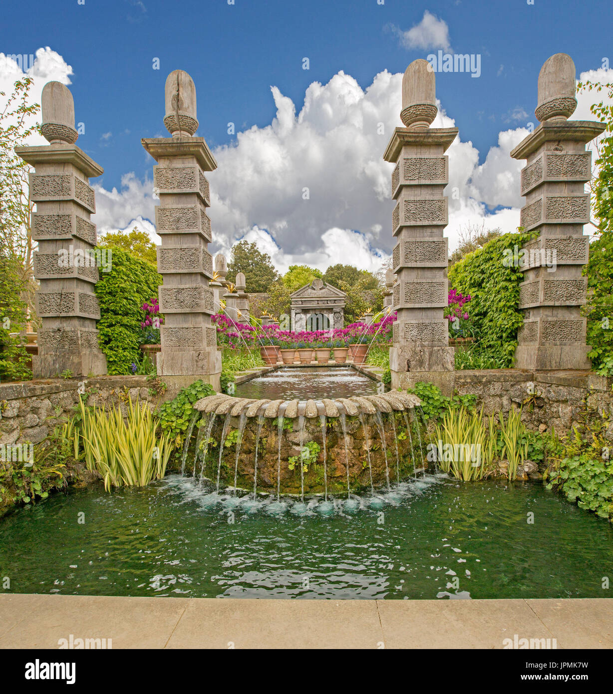 Große, dekorative und außergewöhnliche Wasserspiel mit riesigen geschnitzten Holz Säulen, symmetrische Ströme von Wasser über Stein Wand läuft, und rote Tulpen Stockfoto