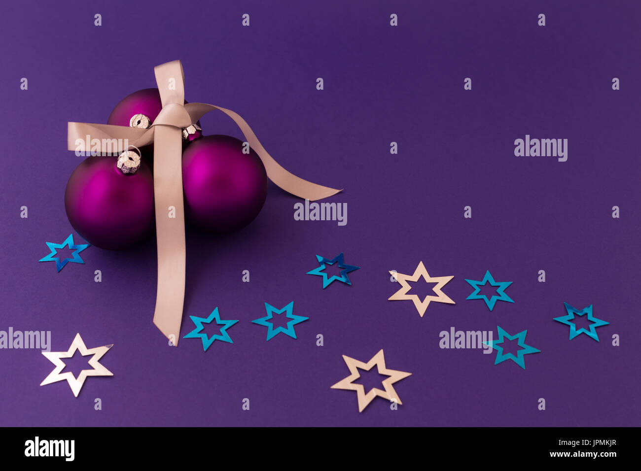 Schöne lila Weihnachtskugeln mit satin-Effekt, graue Geschenkband und metallische silberne und blaue Sterne auf lila Hintergrund. Stockfoto