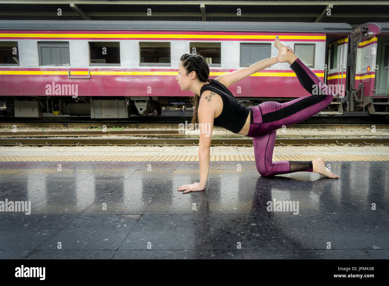 Gesunde Frau, die Yoga macht, posiert draußen auf dem Boden eines Bahnhofs in Asien und trägt bunte Fitnesskleidung Stockfoto