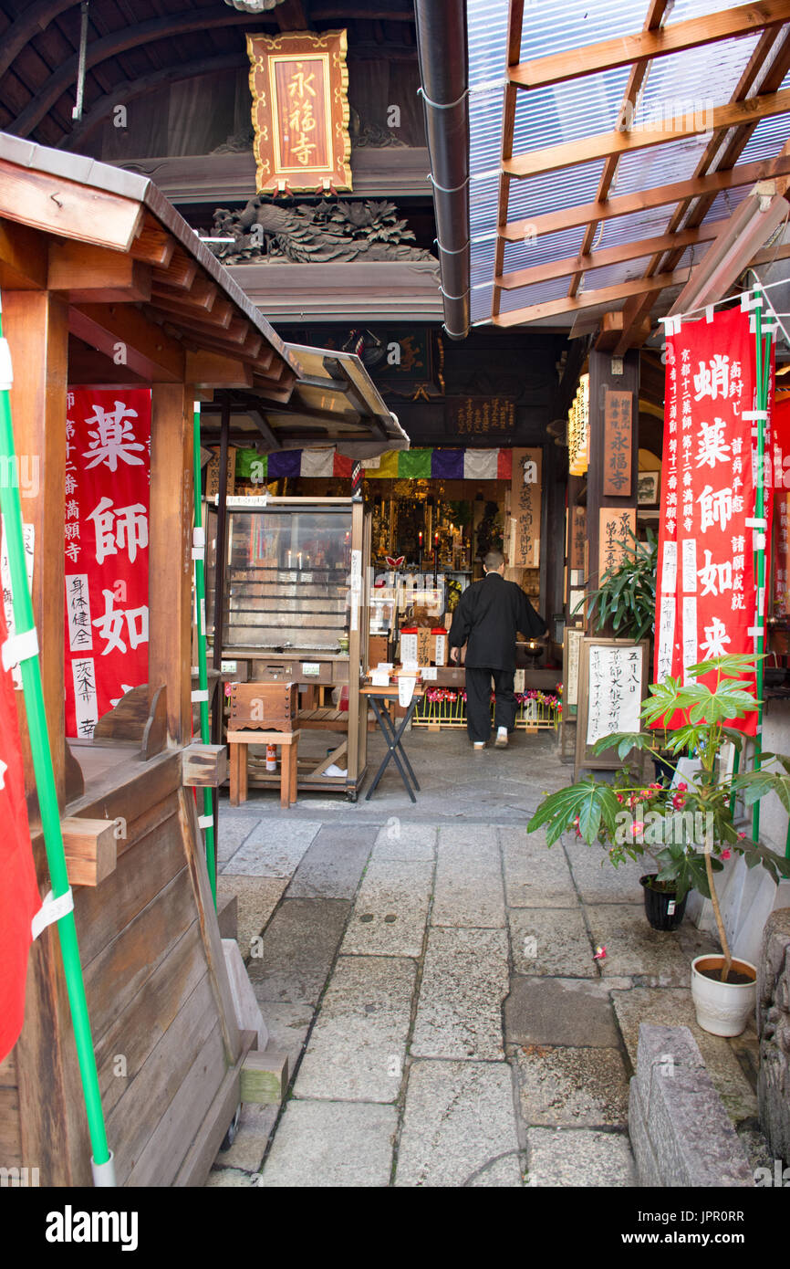 Eine Person gekleidet in schwarz an der gemeinsam-gu-Schrein in Kyoto. Bunte Fahnen schmücken den Ort der Anbetung. Stockfoto