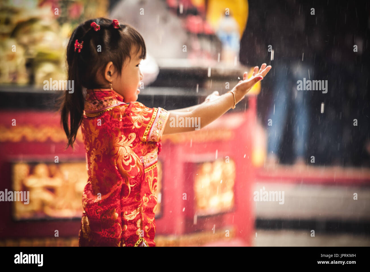 Junge chinesische Mädchen mit Händen nach außen verfangen der Tropfen Regen während der Feierlichkeiten zum Chinesischen Neuen Jahr in einem buddhistischen Tempel in Bali. Stockfoto