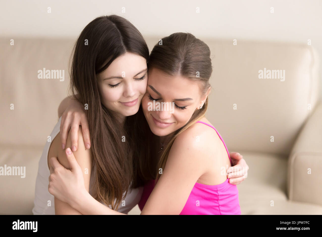 Zwei junge Frauen Freunde sanft umarmt auf sofa Stockfoto