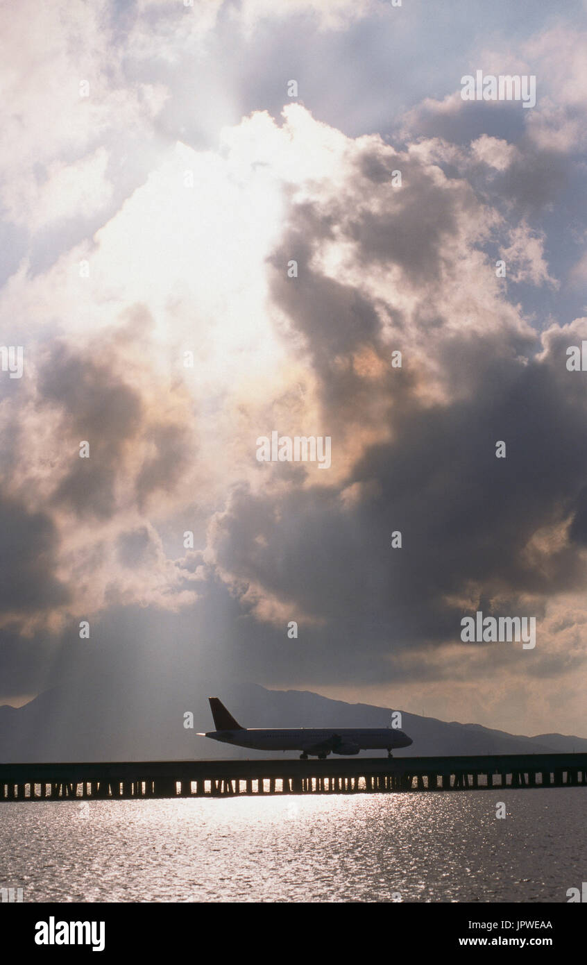 generische Airbus A321-100 Rollen über Damm Rollweg über dem Meer mit Sonnenstrahlen, Sonne glitzerte aus dem Wasser und Wolken hinter Stockfoto