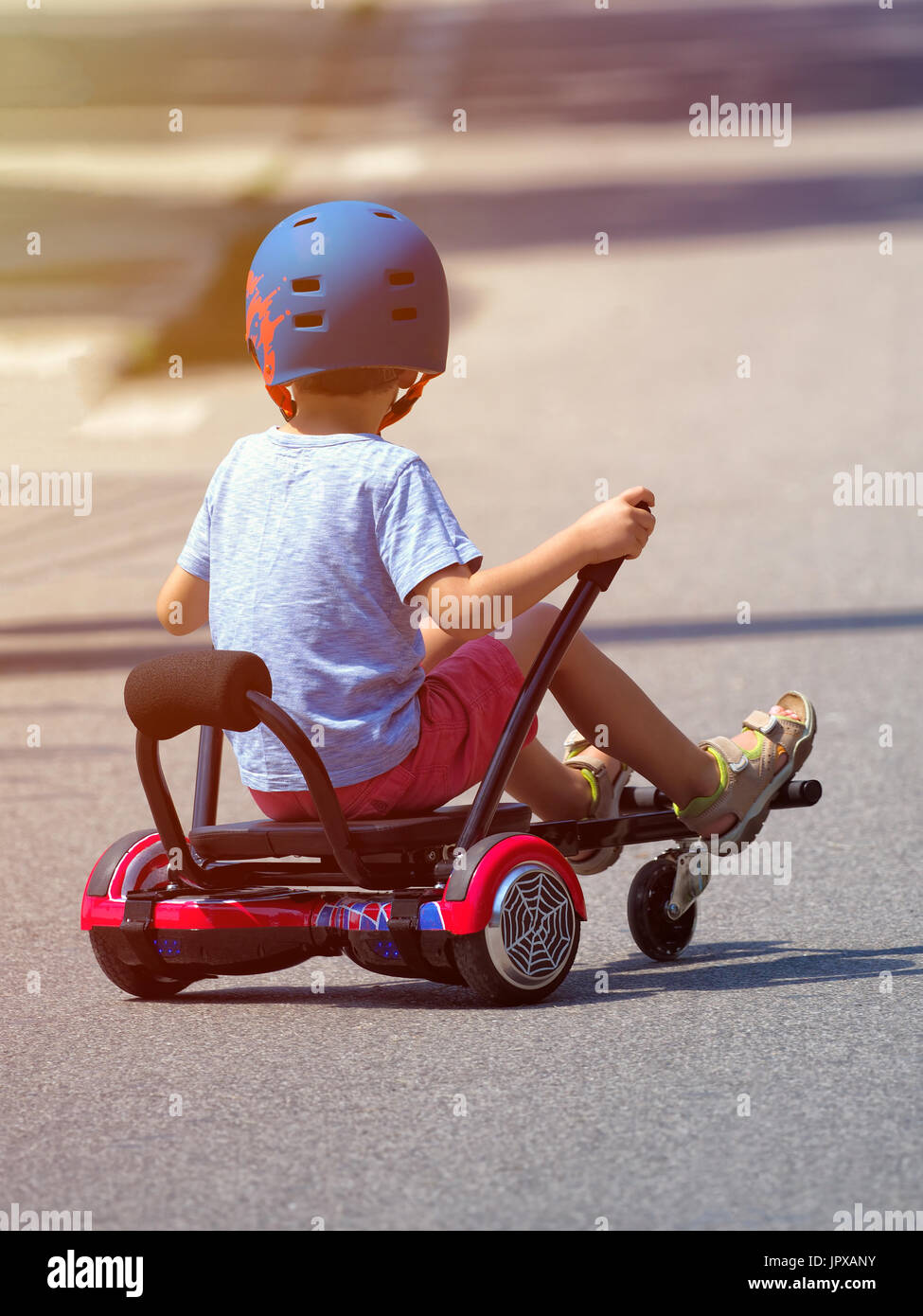 Fröhlicher Junge auf Hoverboard oder Gyroscooter mit Kart-Zubehör-Kit im Freien stehen. Neue moderne Technologien Stockfoto