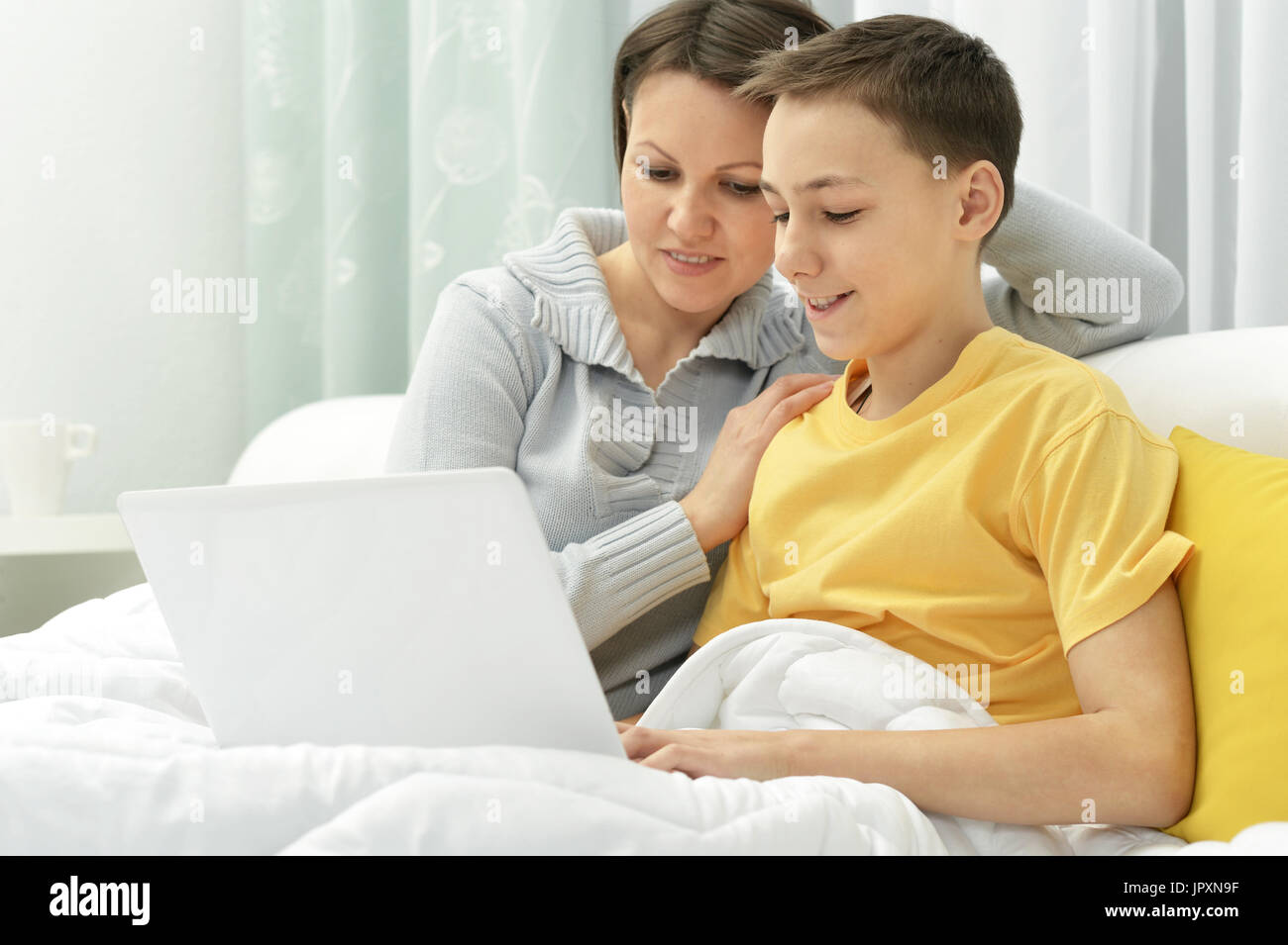 Mutter und Sohn sitzen auf schlecht und mit laptop Stockfoto
