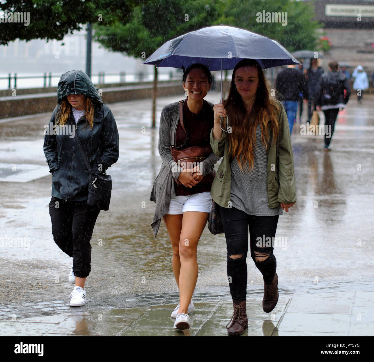 Zwei junge Frauen, die gemeinsame Nutzung von einem Sonnenschirm, während man bei starkem Regen in London, England Stockfoto