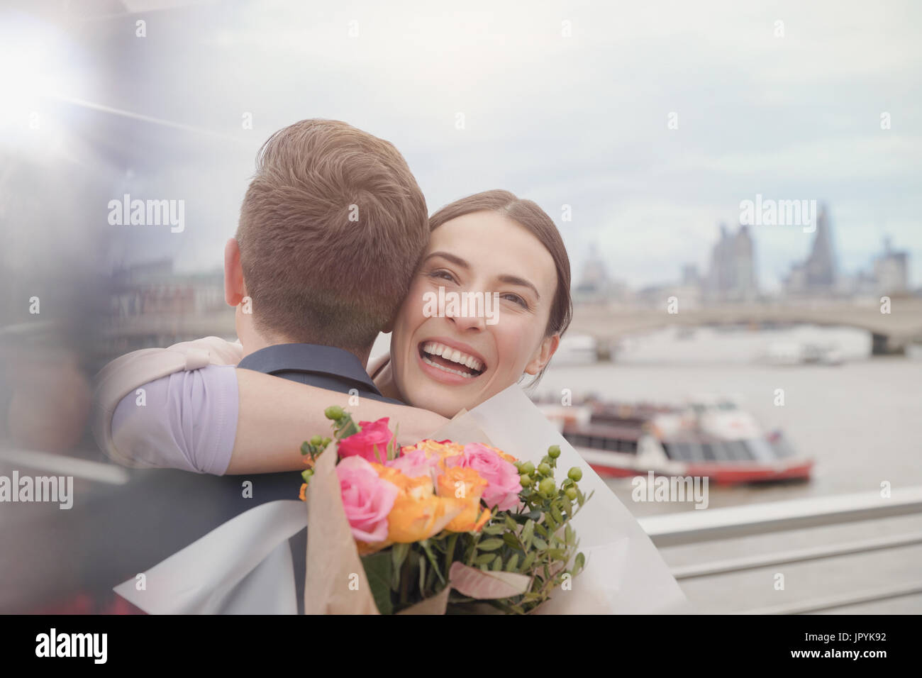 Glücklich, dankbar Frau blumeblumenstrauß empfangen, umarmt Freund an städtischen Uferpromenade Stockfoto