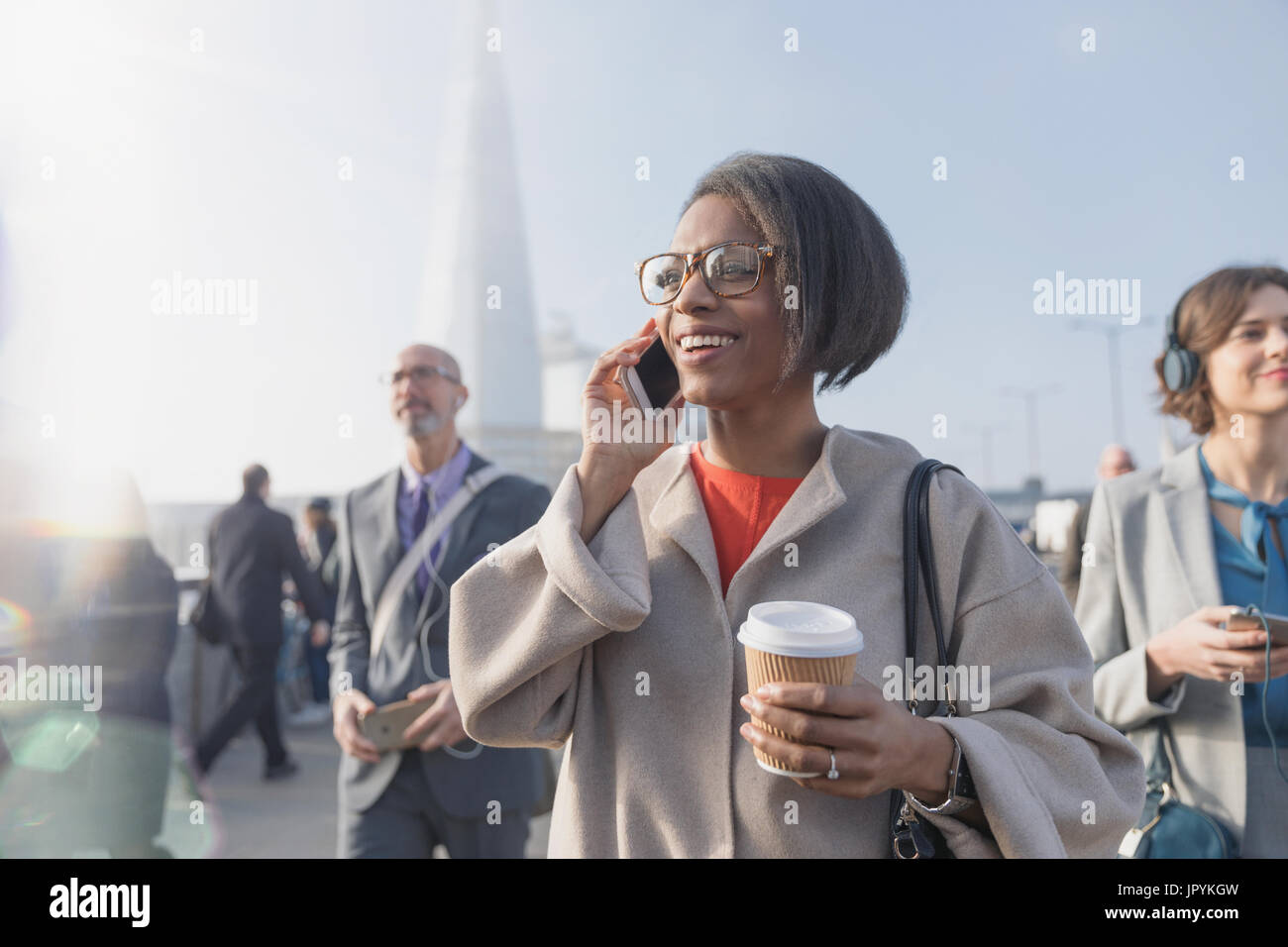 Lächelnd Geschäftsfrau Kaffee trinken und reden über Handy auf sonnigen belebten städtischen Fußgängerbrücke Stockfoto