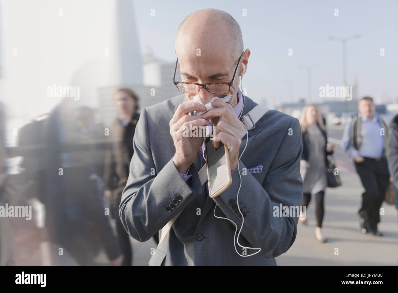 Geschäftsmann Nase mit Gewebe, hält Handy und Kopfhörer auf städtischen Fußgängerbrücke Stockfoto