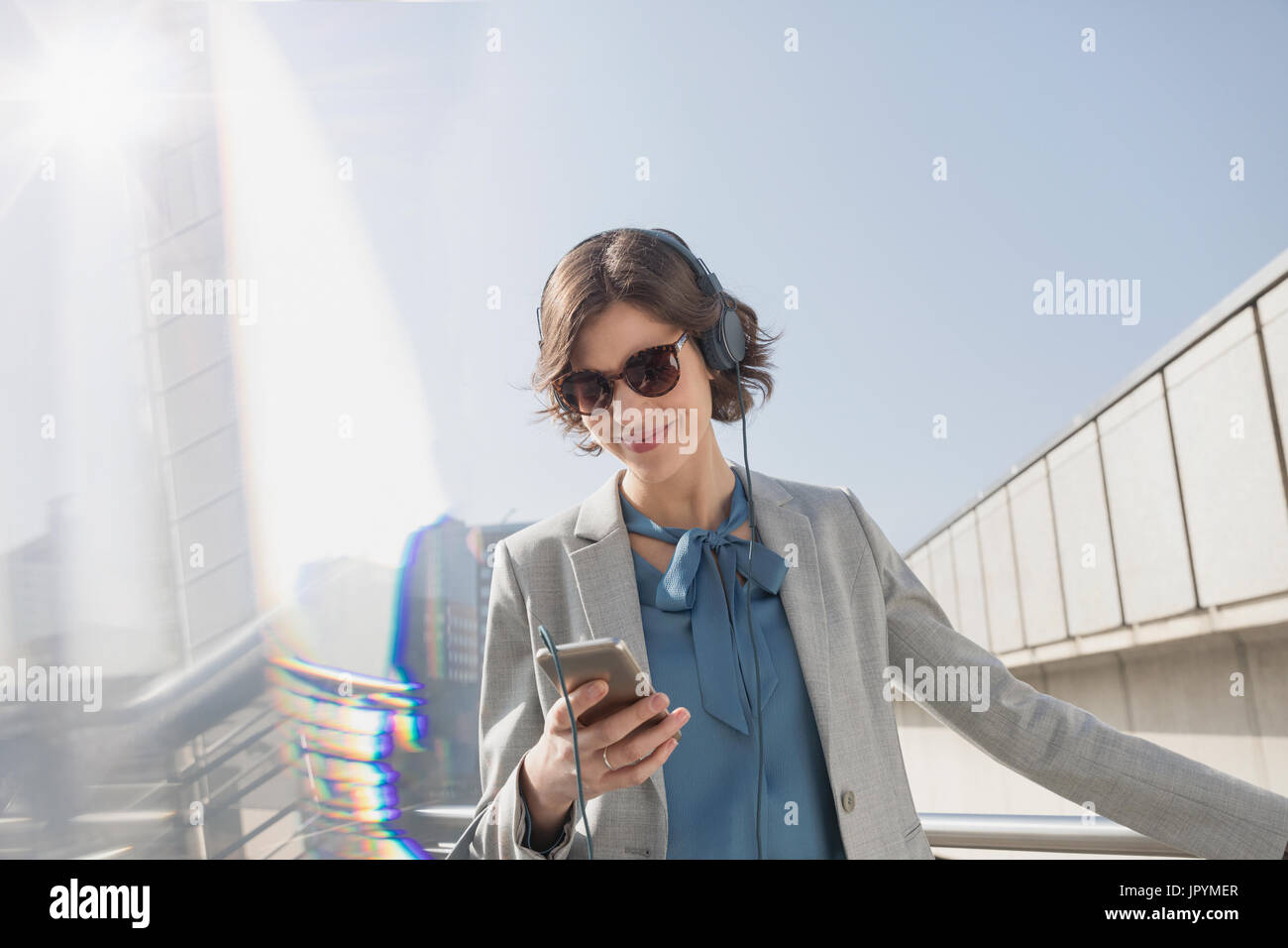 Lächelnd Geschäftsfrau mit Sonnenbrille Musikhören mit Smartphone und Kopfhörer Stockfoto