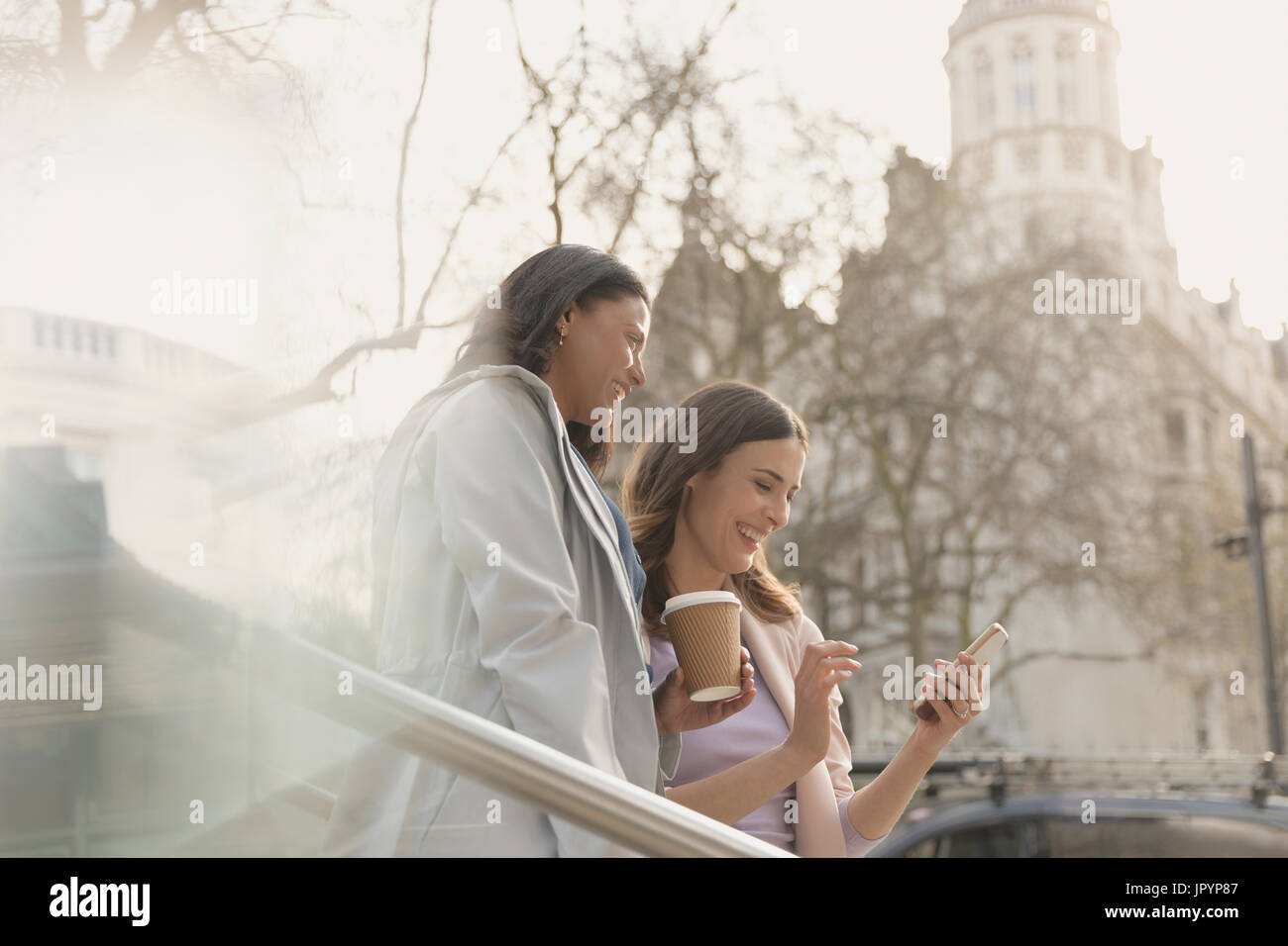 Lächelnden Freundinnen Kaffee trinken und mit Handy in Stadt Stockfoto