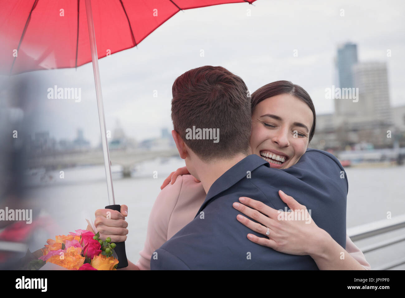 Lächelnd, liebevolle paar mit Sonnenschirm und Blumen umarmt auf städtische Brücke, London, UK Stockfoto