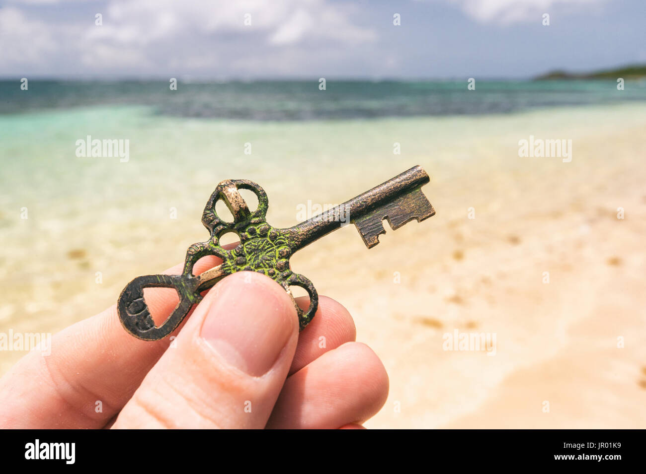 Hand, die einen Schatz-Schlüssel auf einem tropischen Strand gefunden. Chance oder Mystery-Konzept. Stockfoto