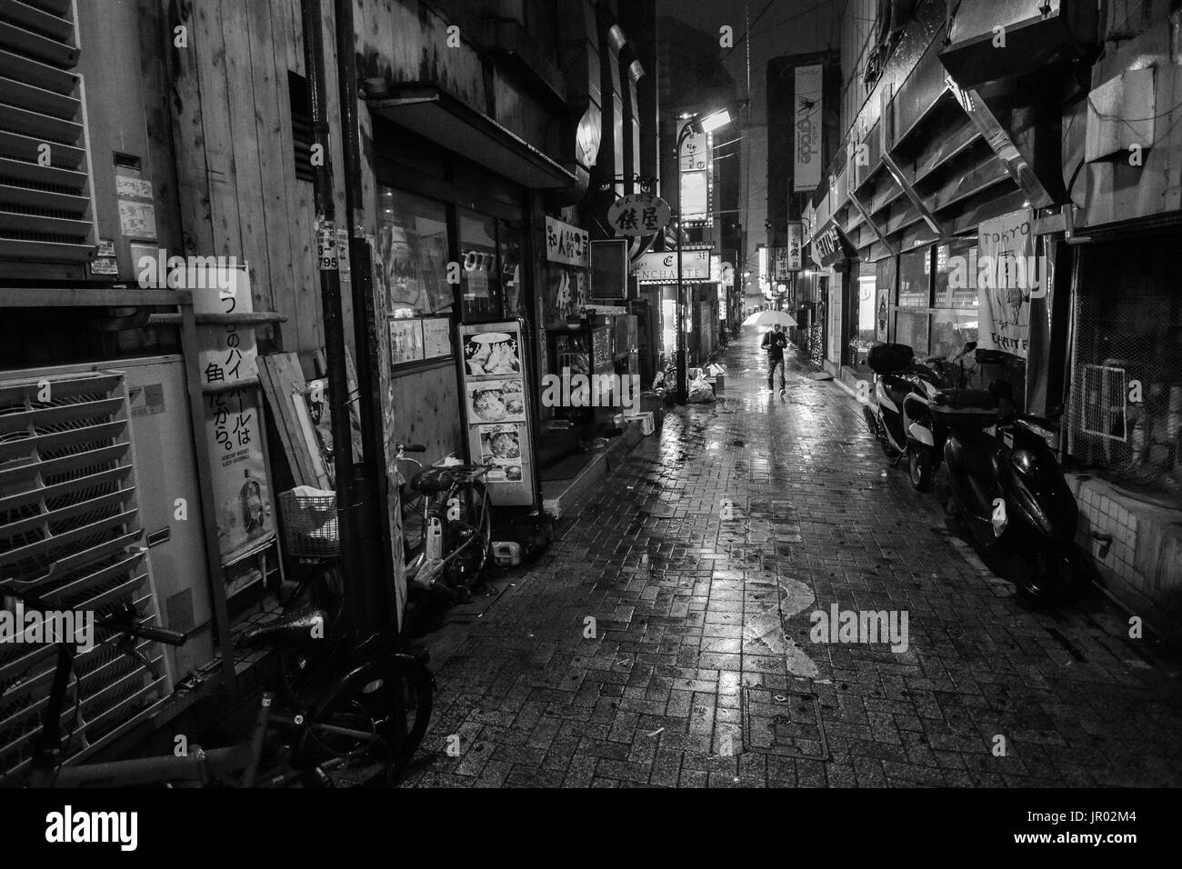 TOKYO, JAPAN - 8. APRIL 2017 - Schwarz und Weiß von einem Mann mit einem Regenschirm auf eine einsame Gasse in einer regnerischen Nacht in Tokyo City Stockfoto