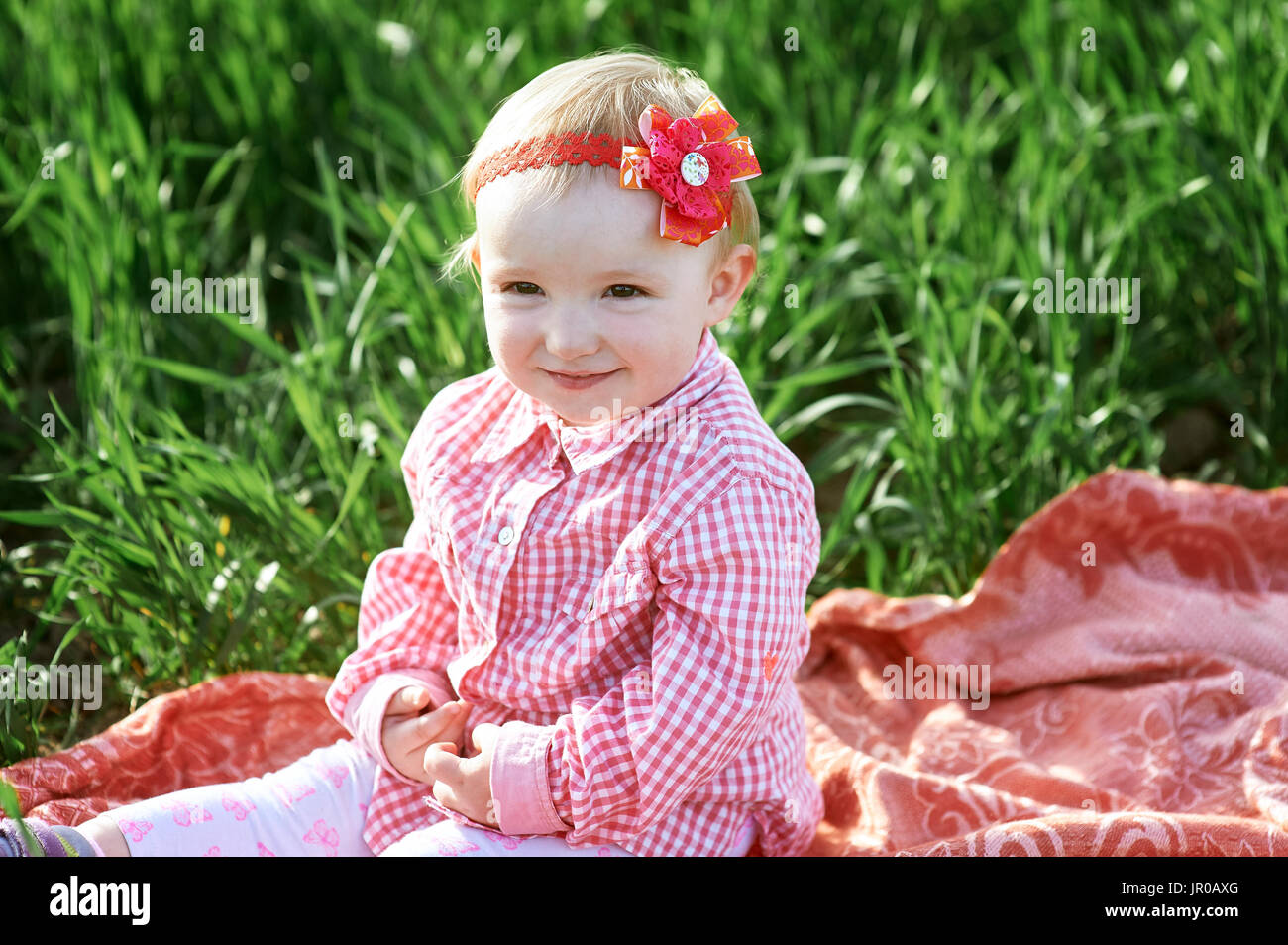 Kleines Mädchen sitzt auf einer Decke in der Sommerwiese Stockfoto