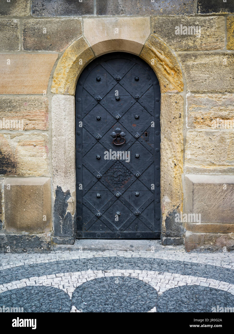 Eine gewölbte Metalltür In einem Steinblock Wand mit dekorativen Pflastersteine in einem Design; Prag, Tschechische Republik Stockfoto