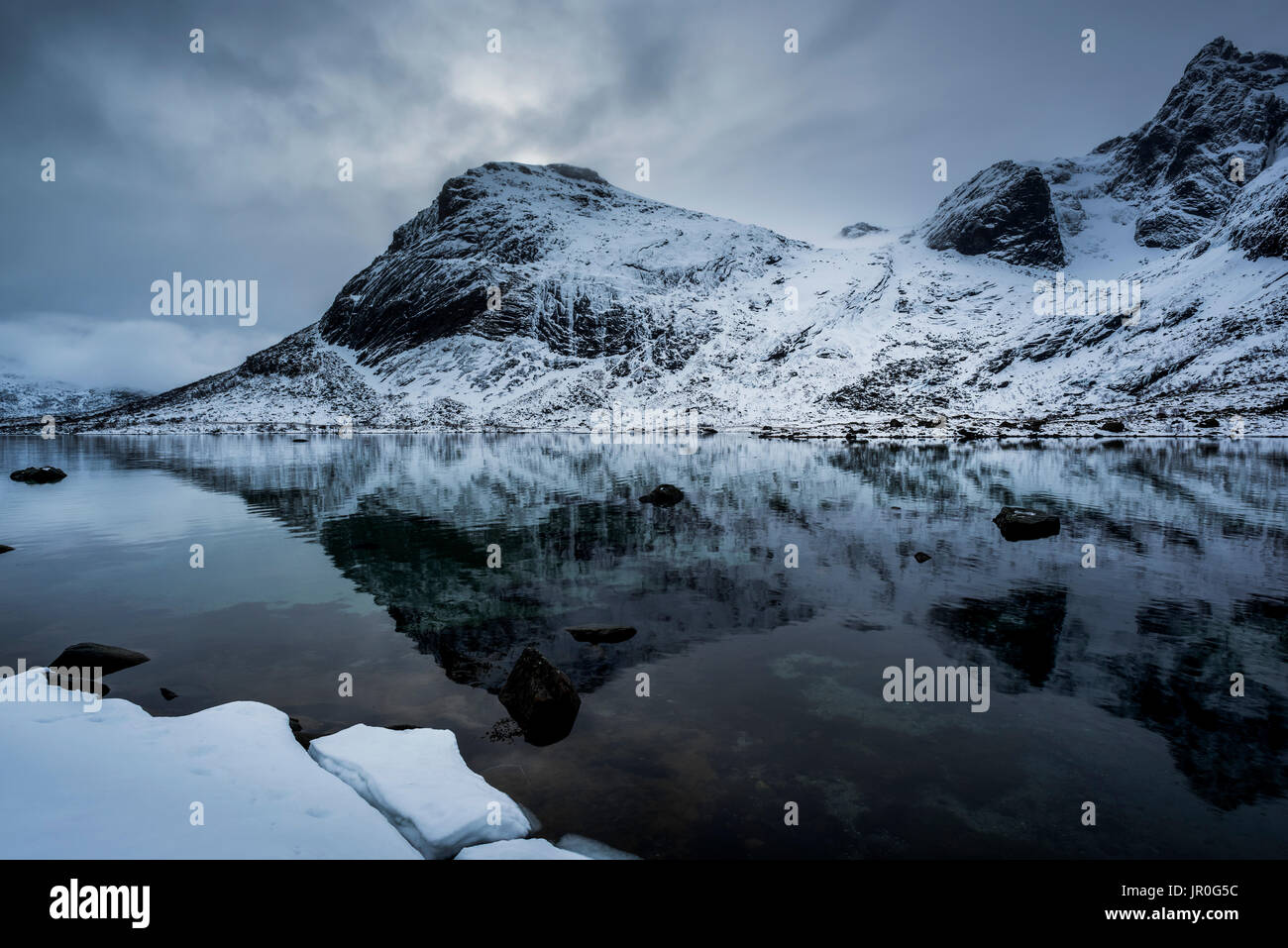 Landschaft der schroffen, schneebedeckten Berge im ruhigen Wasser des Ozeans reflektiert; Lofoton Inseln, Nordland, Norwegen Stockfoto