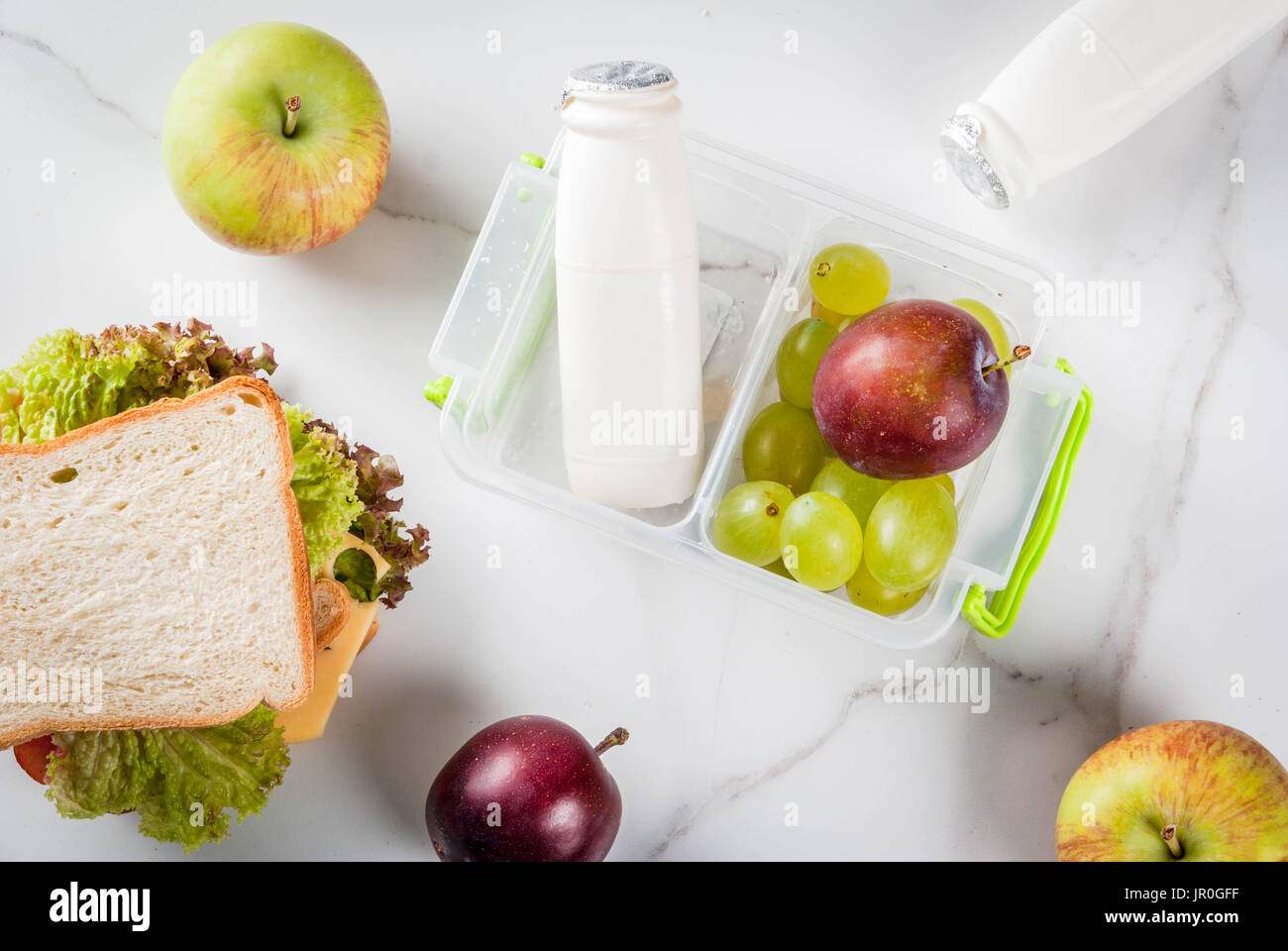 Zurück zur Schule. Ein gesundes Mittagessen in einer Box ist frisches Obst (Äpfel, Pflaumen, Weintrauben), eine Flasche Joghurt und ein Sandwich mit Salat, Tomaten, Käse, mea Stockfoto