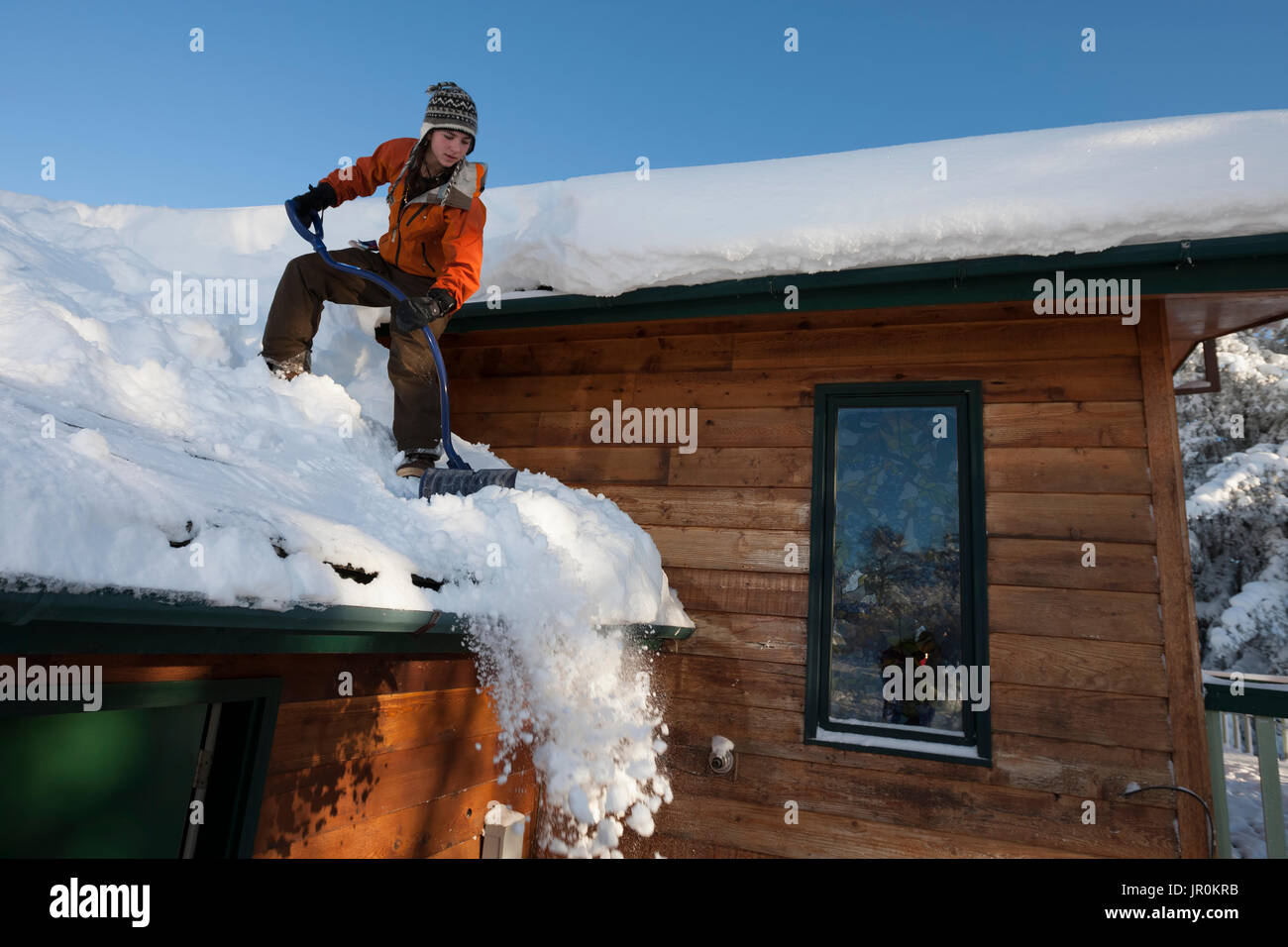 Eine junge Frau entfernt Schnee vom Dach Ihres Hauses, Homer, Alaska, Vereinigte Staaten von Amerika Stockfoto