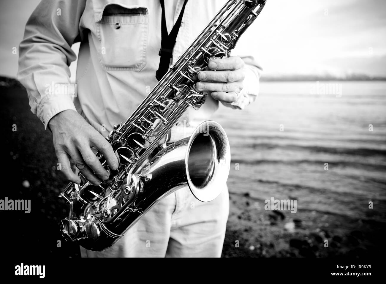 Ein Mann steht ein Saxophon spielen, am Strand am Rand des Wassers, Alaska, Vereinigte Staaten von Amerika Stockfoto
