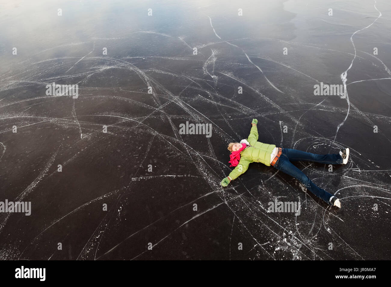 Eine junge Frau legt sich auf den Rücken auf einer gefrorenen Oberfläche, die beim Eislaufen, Alaska, Vereinigte Staaten von Amerika Stockfoto