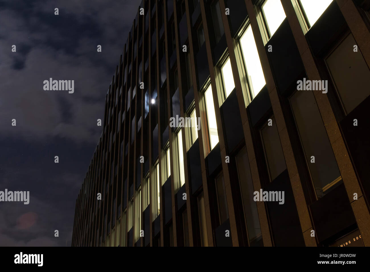 Nachtansicht der Fassade eines modernen Gebäudes in Frankfurt am Main. Wolken und Vollmond spiegeln sich auf Gläser. Stockfoto