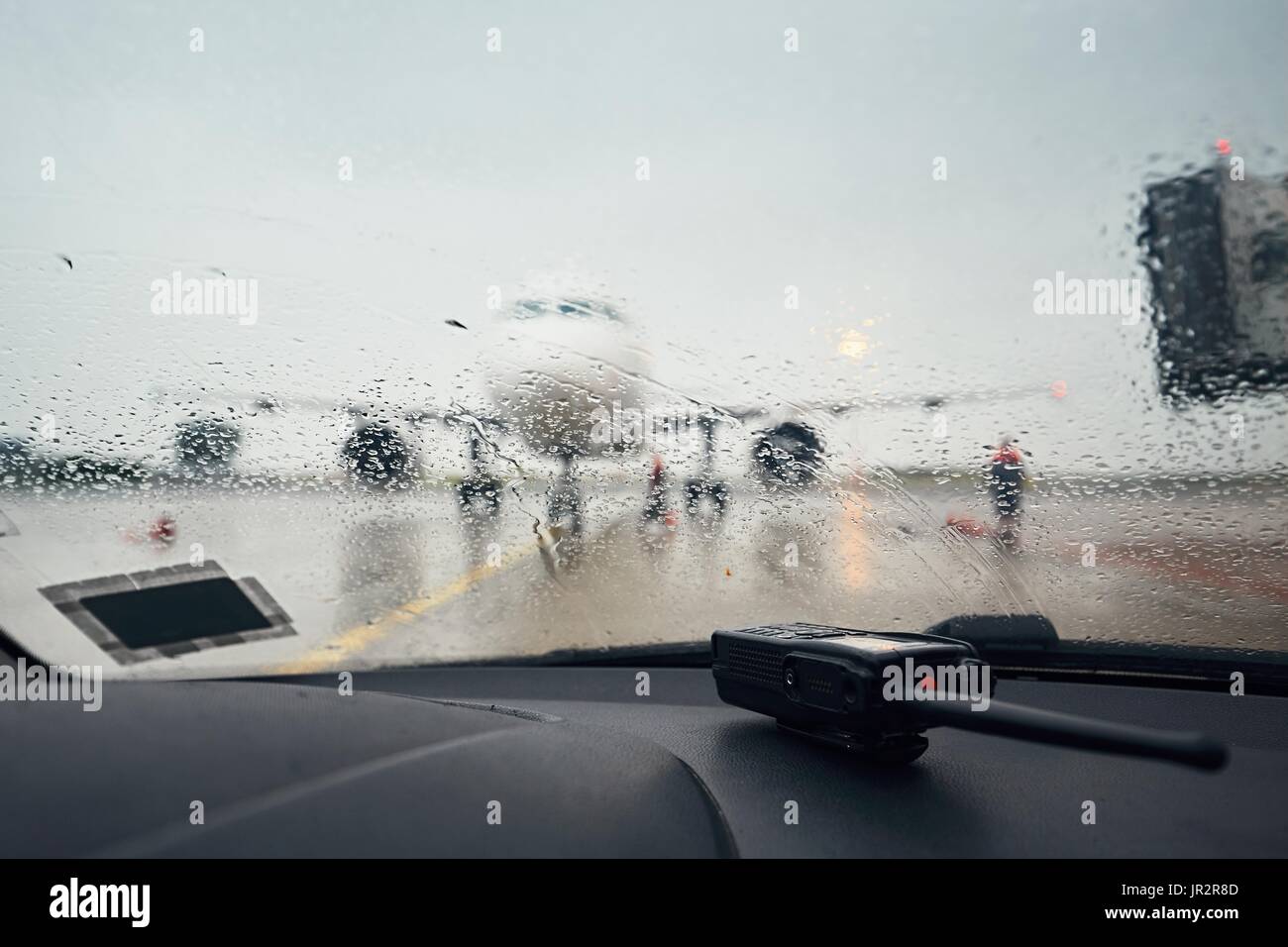 Ein geschäftiger Flughafen im Regen. Ein Blick durch eine nasse Fenster im Flugzeug vor dem Flug. Stockfoto