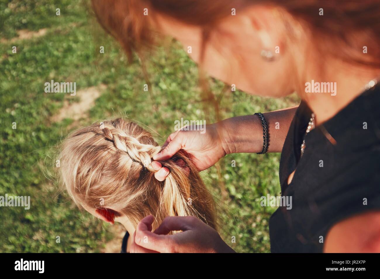 Junge Frau Haarflechten des kleinen Mädchens auf dem Garten auf dem Lande machen. Stockfoto