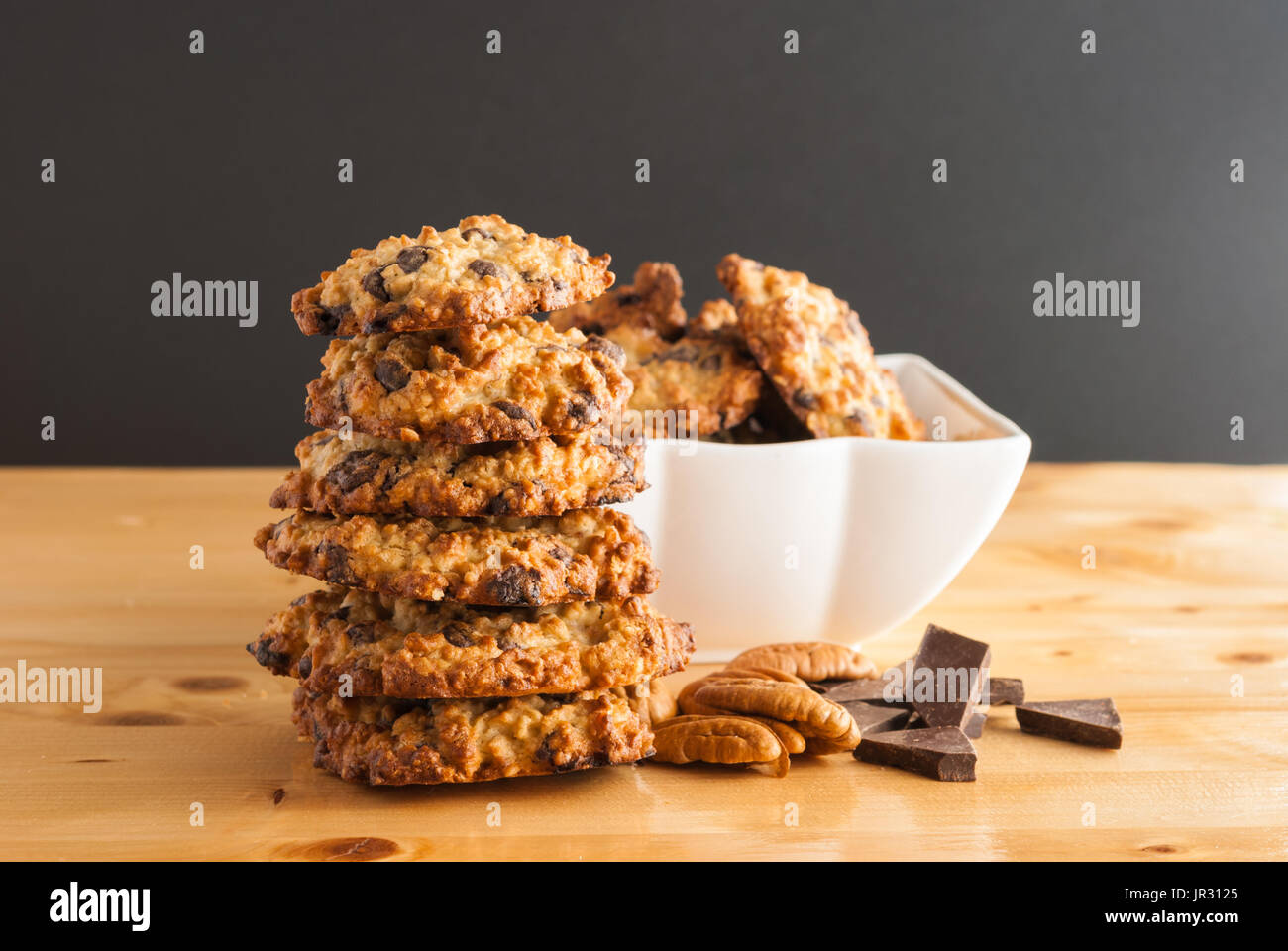 Gestapelt, Schokoladenkekse, weiße Schüssel mit Cookies, Pecan und Stücke von Schokolade auf einem schwarzen Hintergrund Stockfoto