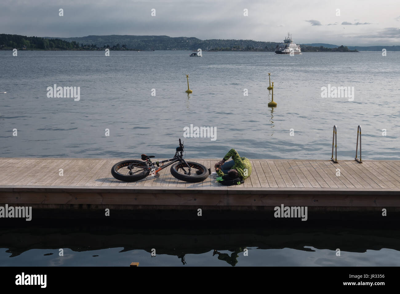 Oslo, Norwegen - Mann 20. Mai 2017 - neben seinem fetten Motorrad hinlegen und überprüft seine Telefon auf hölzernen Steg im Oslofjord an sonnigen Sommertag Stockfoto