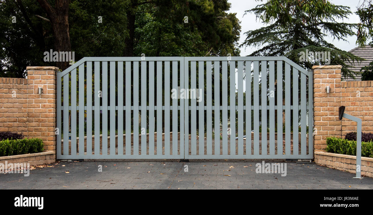Metall-Einfahrt Eingangstore inmitten einer Ziegelmauer mit Garten Bäume im Hintergrund Stockfoto