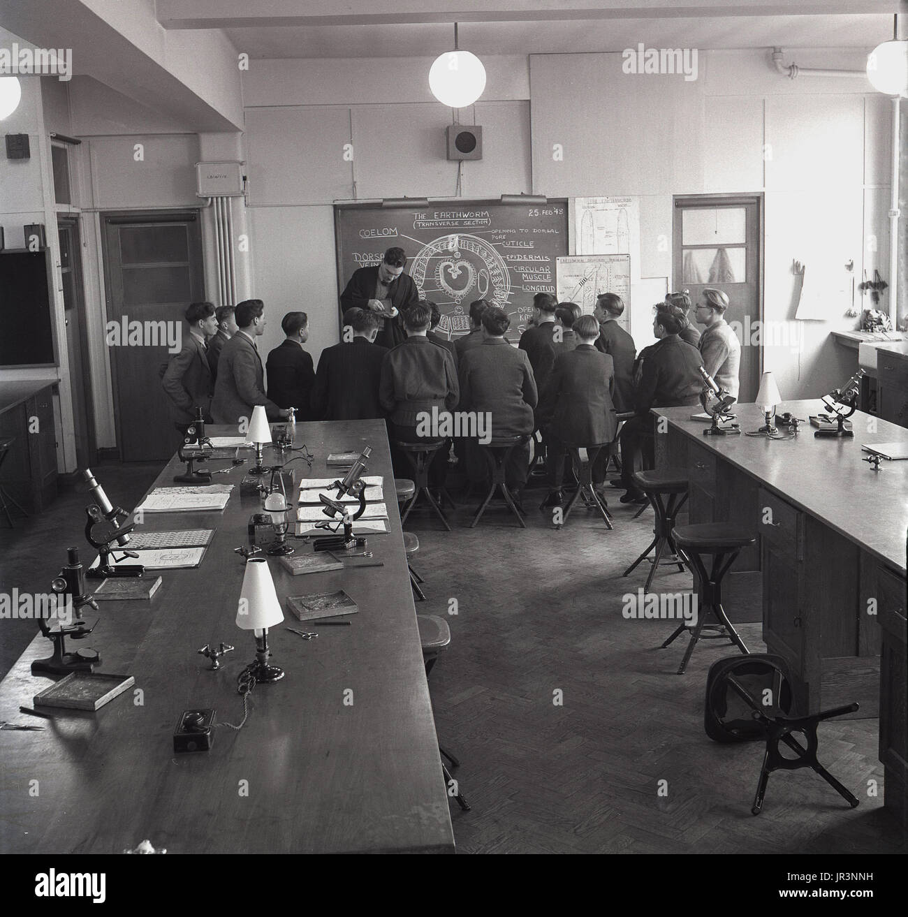 1950, historische, Wissenschaft Kategorie Regenwürmer studieren, eine Gruppe von männlichen Studenten sitzen auf Hockern an der Vorderseite der Klasse durch die Tafel als Lehrerin zeigt Ihnen Proben, England, UK. Stockfoto